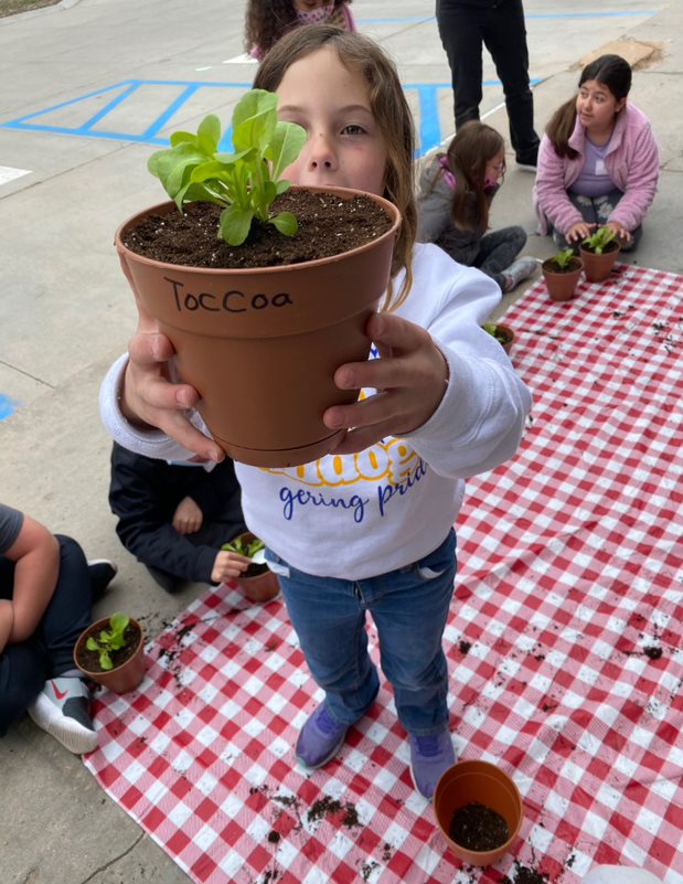 a child holds up a potted plant as other children put plants in pots in the background