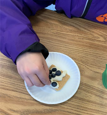 a child decorates a graham cracker with fruit