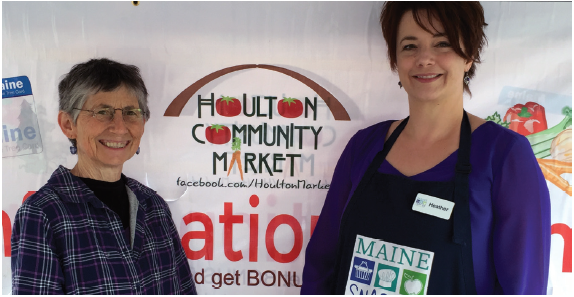 Two nutrition educators standing in front of a banner that says "Houlton Community Market".