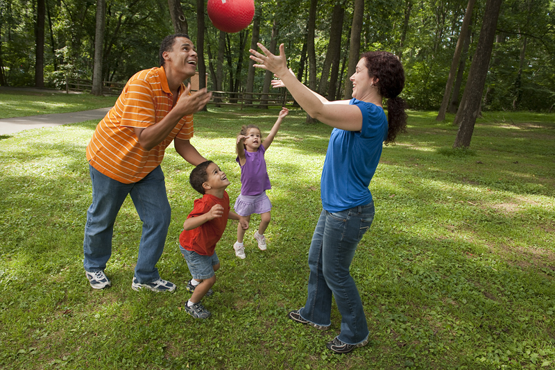 Parents with two young children play outside with a handball