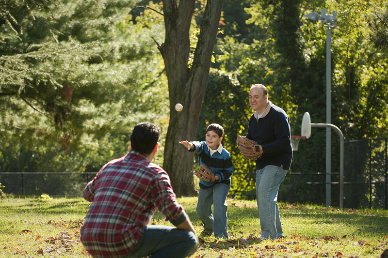 A boy plays baseball with his father and grandfather in a park