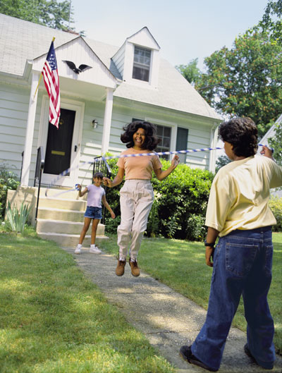 A mom and two children jumping rope in the front yard