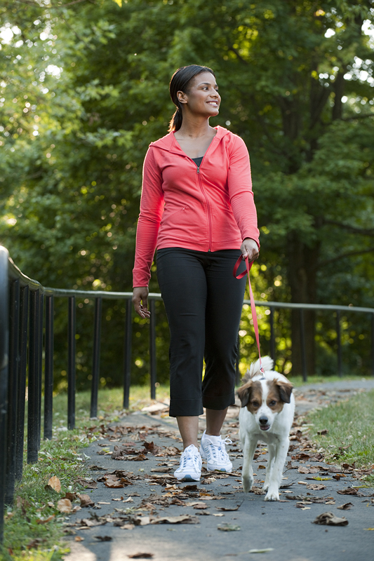 A woman walking her dog on an paved walking path