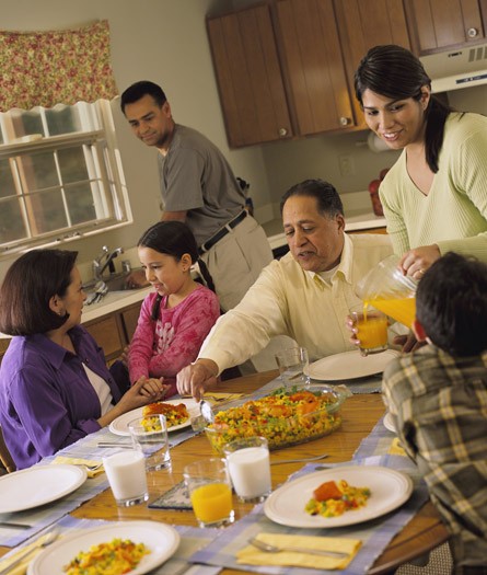A Latino family of six (mother, father, two young children and grandparents) sitting around a table kitchen table for dinner.