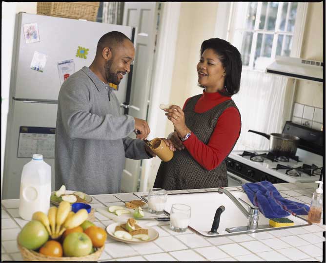 A man and pregnant woman snack on apples with peanut butter
