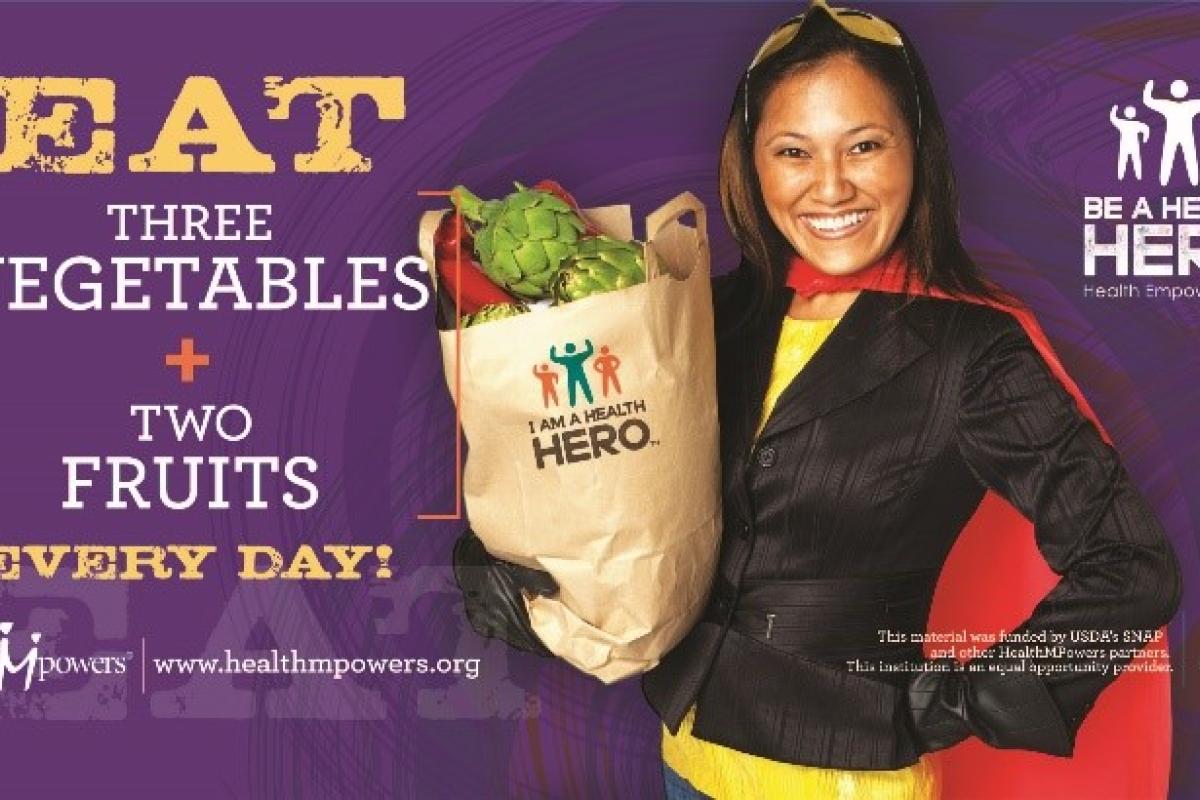 Eat three vegetables + two fruits Every Day! Be a Healthy HERO with an image of a woman wearing a cape and holding a bag of fruits and vegetables