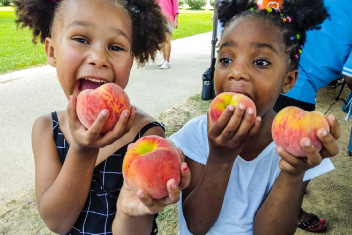 2 girls hold peaches from the Farmers Market