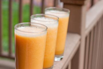 3 glasses of orange drink on a railing