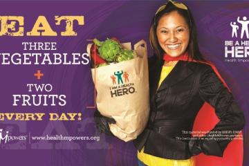 Eat three vegetables + two fruits Every Day! Be a Healthy HERO with an image of a woman wearing a cape and holding a bag of fruits and vegetables