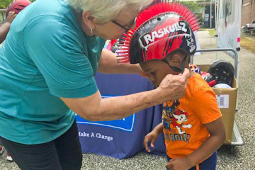 a woman helps a child put on a bike helmet. Live Well Alabama