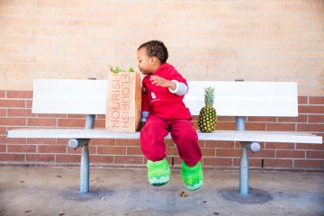 boy sits on a bench with a bag of groceries