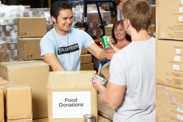 person accepting food donations at a food bank surrounded by card board boxes.