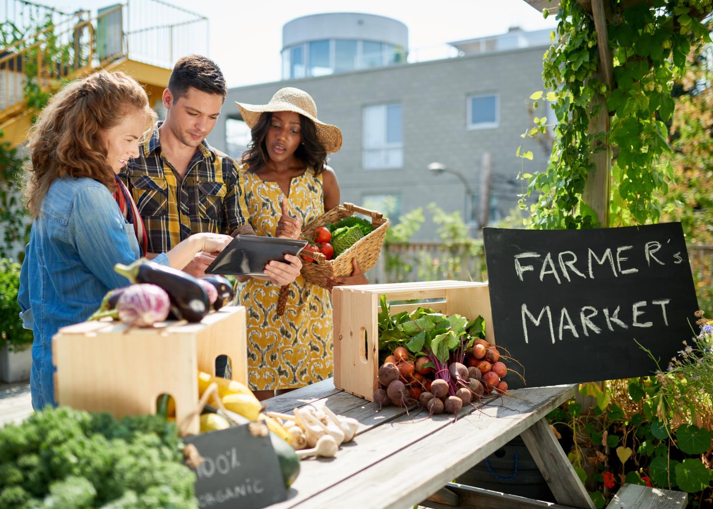 people shopping at a farmers market with a man holding a tablet
