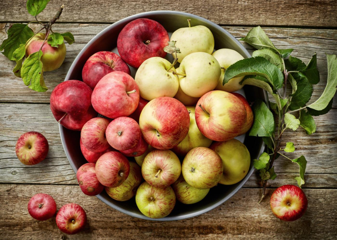 green and red apples in a bowl on a wood background