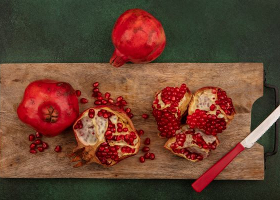 Whole Pomegranates and Cut-Open Pomegranates on a Wooden Cutting Board