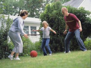 A mother and father kicking a ball in the backyard with their pre-teen daughter