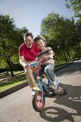 A man helping a young boy learn to ride a bike with training wheels.