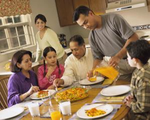 A Latino family of six (mother, father, two young children and grandparents) sitting around a table kitchen table for dinner.