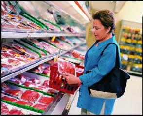 A woman holding a package of ground beef in the meat section of a grocery store.