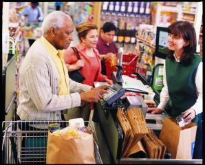 An older adult man checking out at a grocery store and paying with a credit/debit/EBT card.