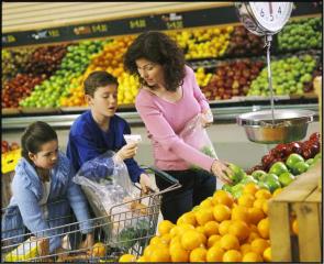 A mother with two pre-teen children using a shopping list and selecting apples in a produce section of a grocery store.